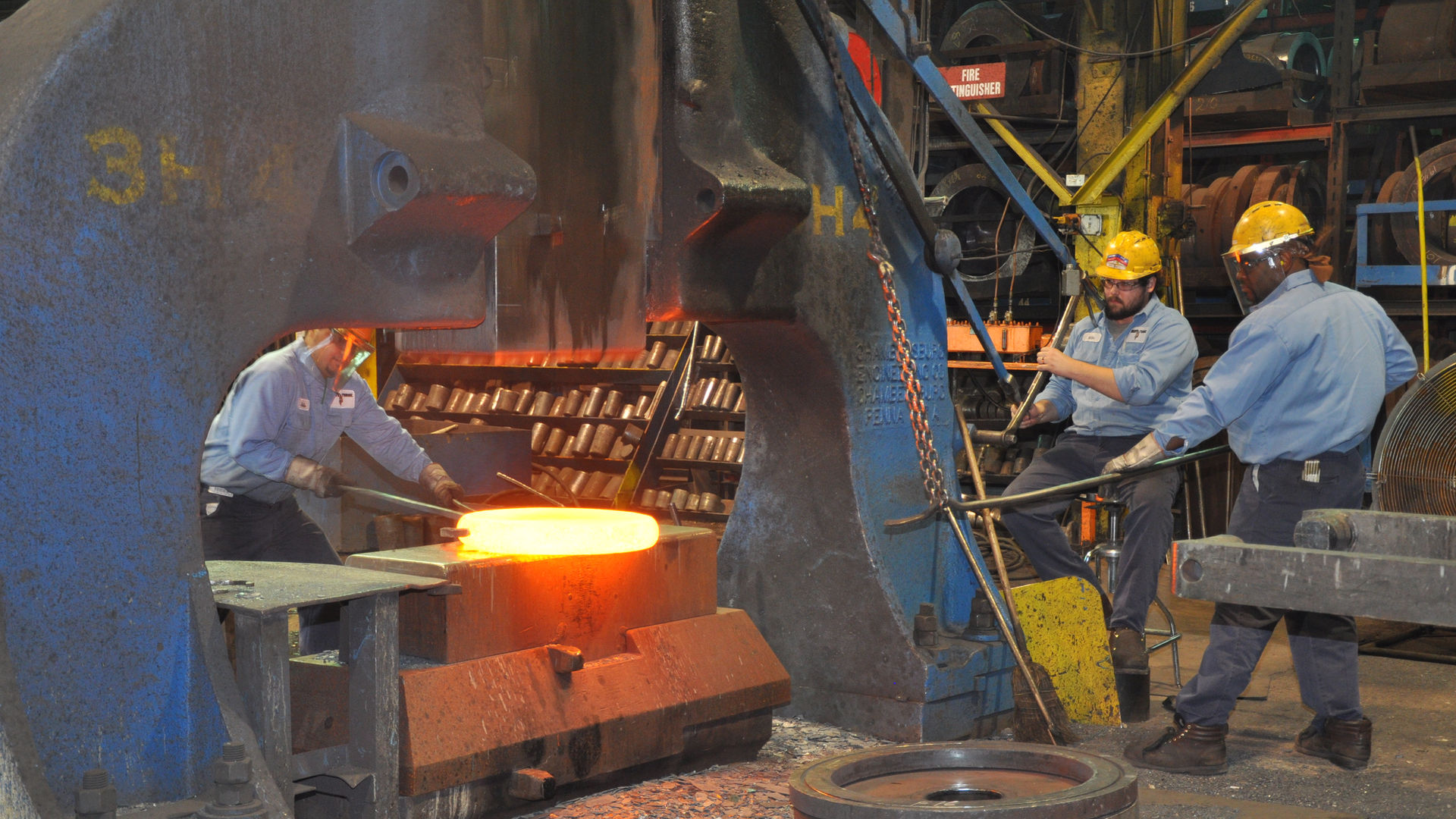 Workers adjusting a hot forging over a hammer