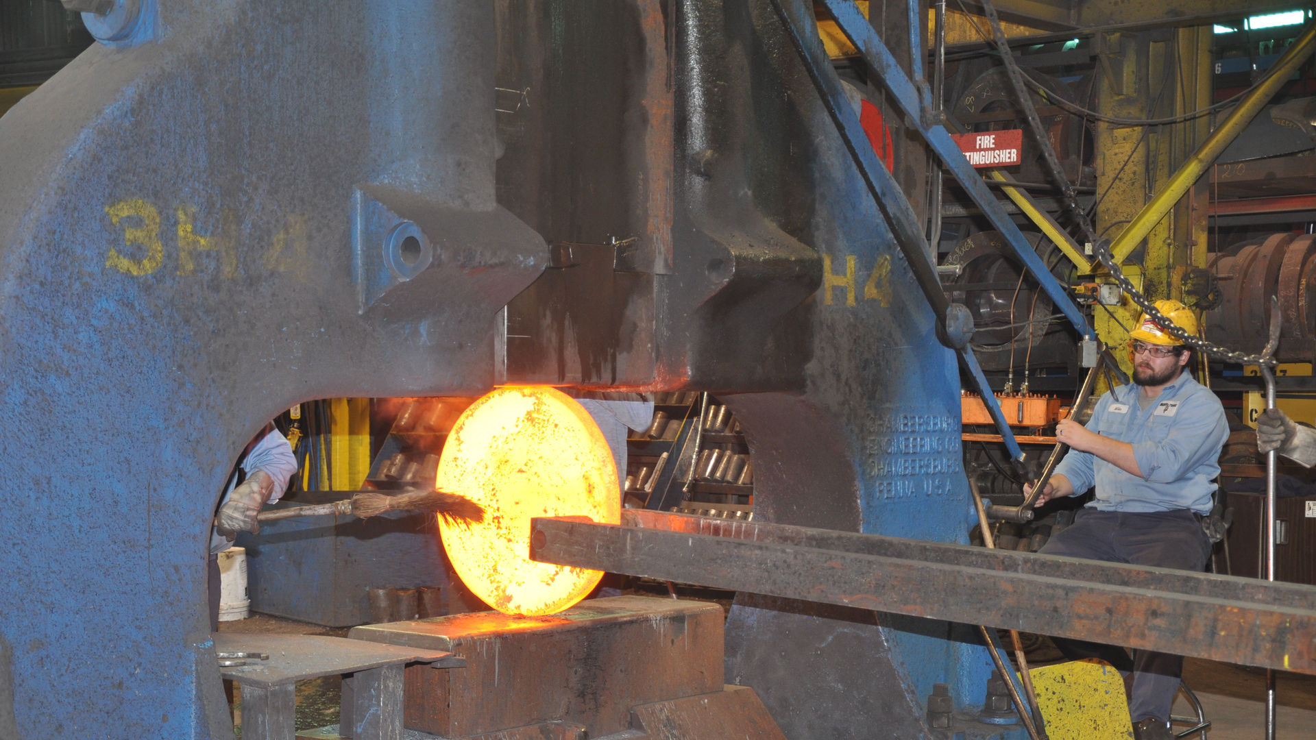 Hot metal disc being forged with a large machine by a workers to smooth out and round the disc at Scot Forge.