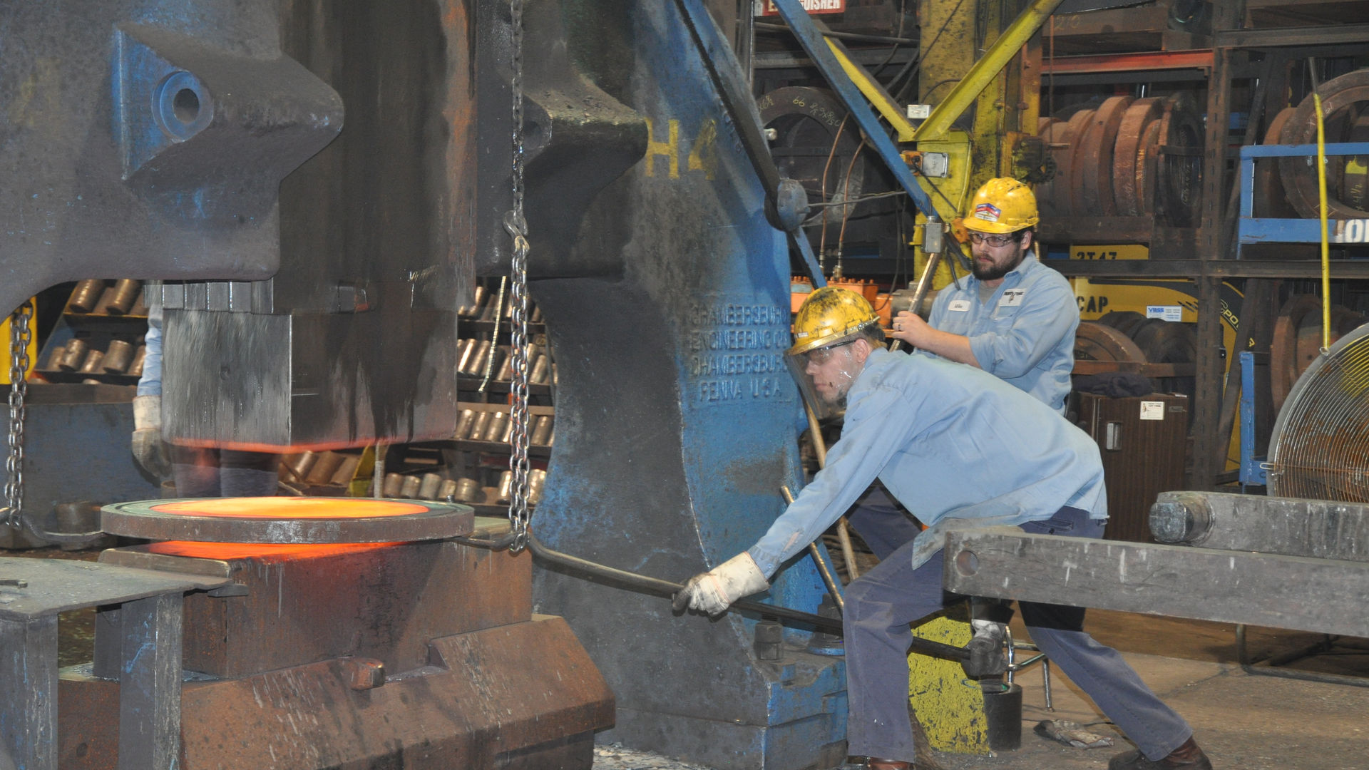 Workers adjusting a hot forging over a hammer